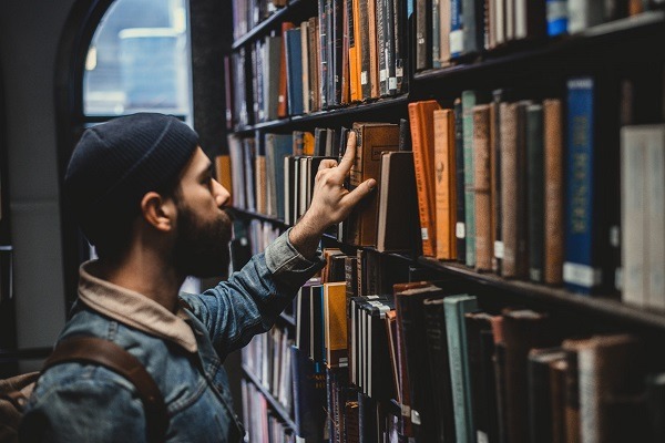 man picking a book from a bookshelf in a library