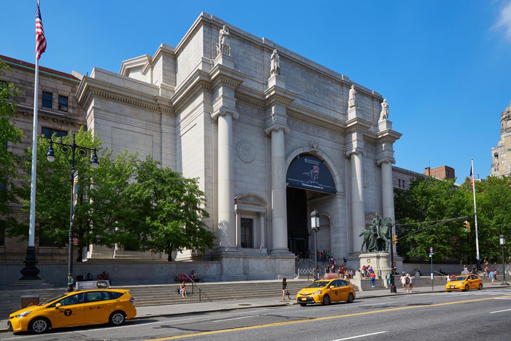American Museum of Natural History building facade with people and yellow taxis
