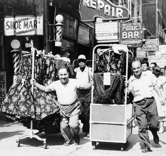 Men pulling racks of clothing on a busy sidewalk in the Garment District in 1955