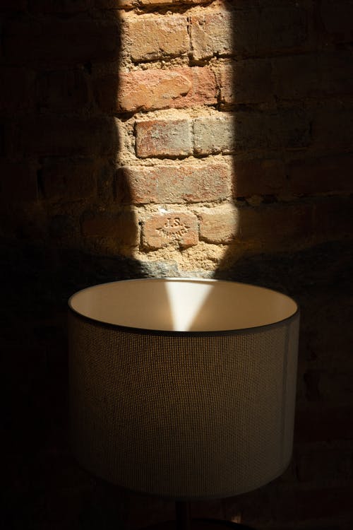  a lampshade near a rough brick wall with shadows in sunlight