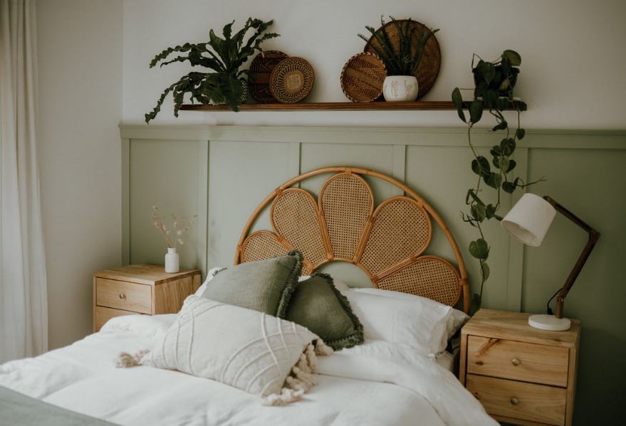 plants on a shelf hanging above a bed, a bedside table with a lamp on top and another bedside table with a vase on top at each side of the bed