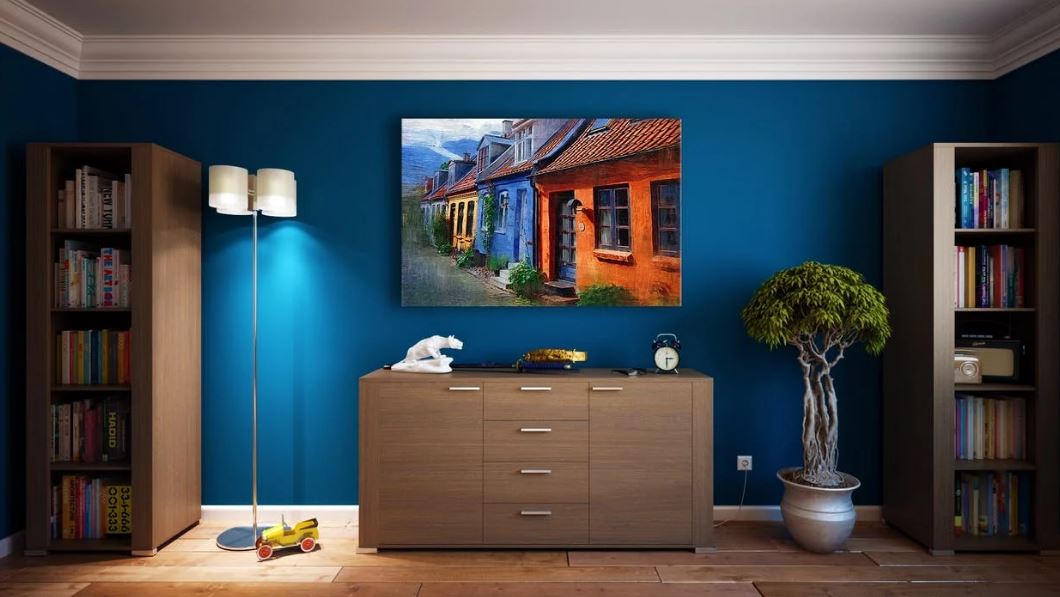 two wooden bookshelves on both left and right sides, a wooden cabinet at the center, blue wall and a painting on the wall, an indoor plant 