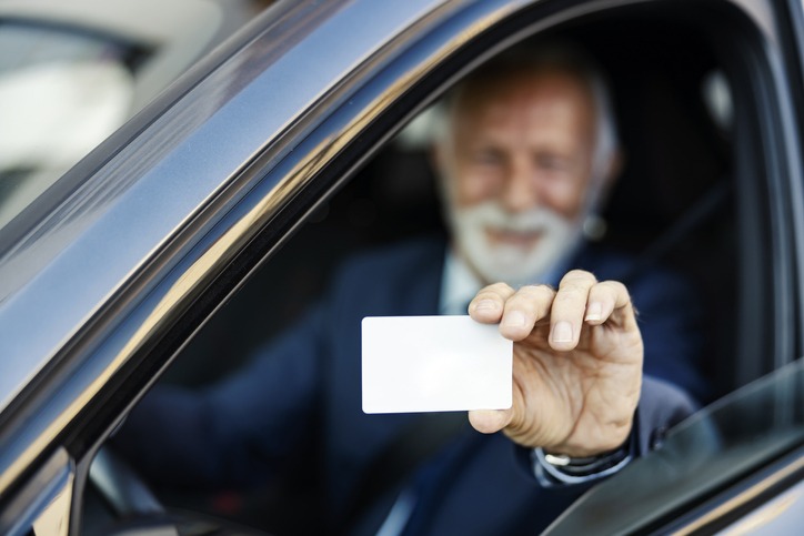 Parking service prepaid card. Close up of a senior businessman sitting in his car and showing his parking service card through the window. Selective focus on hand.