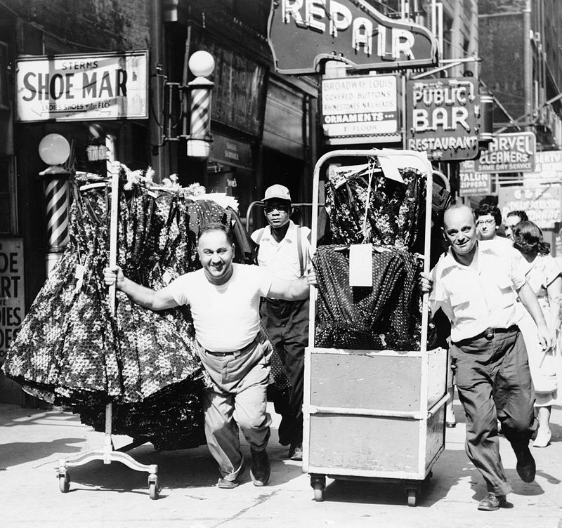 Men pulling racks of clothing on a busy sidewalk in the Garment District in 1955