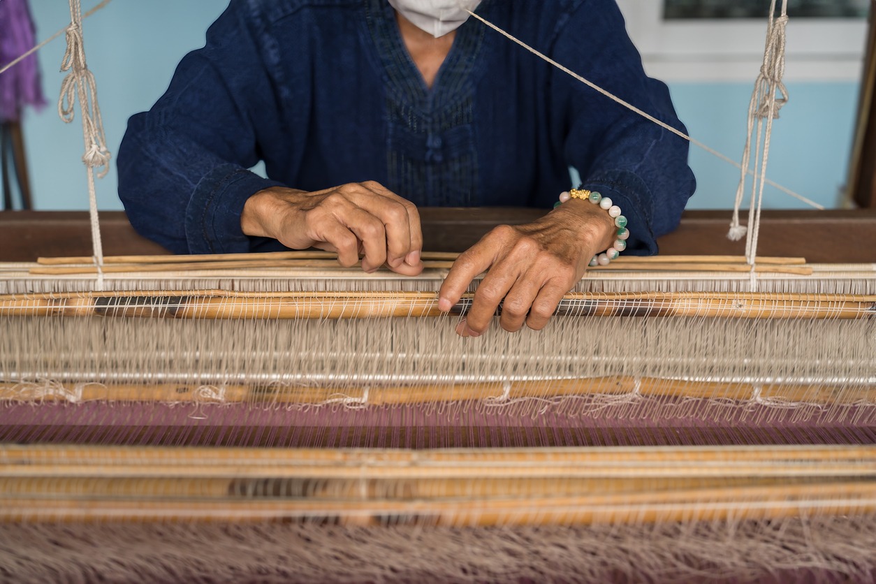 Artisan hands weaving Thai silk on a traditional loom