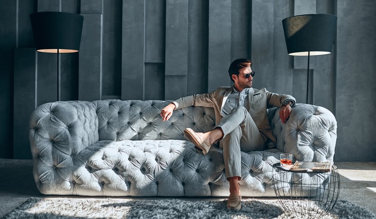 Handsome stylish man in beige suit at home sitting on sofa