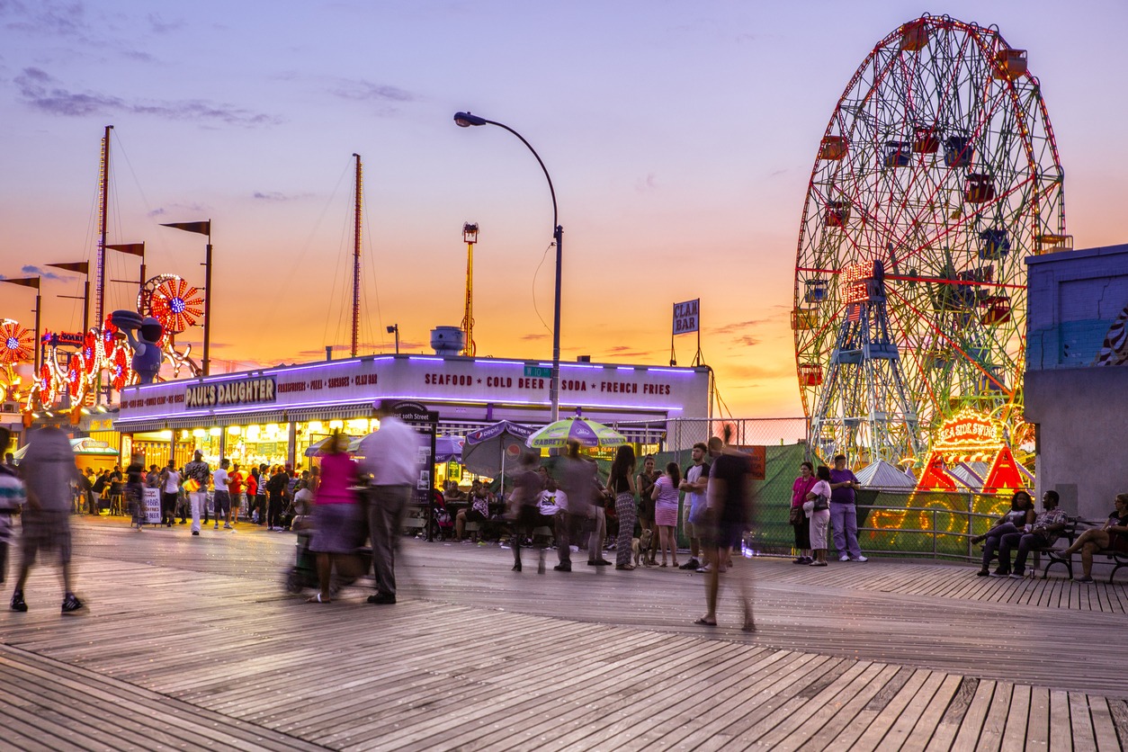a view of the Coney Island’s boardwalk and amusement park with a massive Ferris wheel on the background