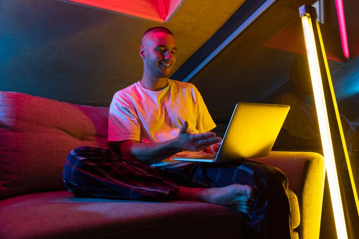 young man sitting at home in neon orange pink lighted room