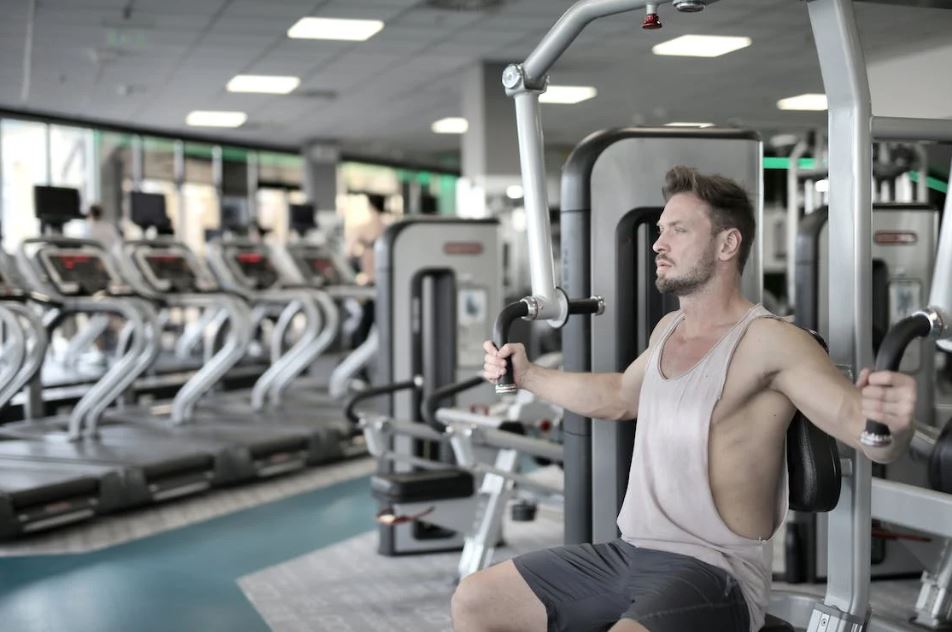 Man in White Tank Top and Grey Shorts Sitting on Exercise Equipment