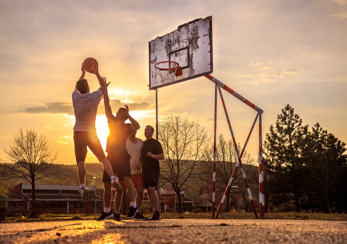 four men playing Street basketball at sunset